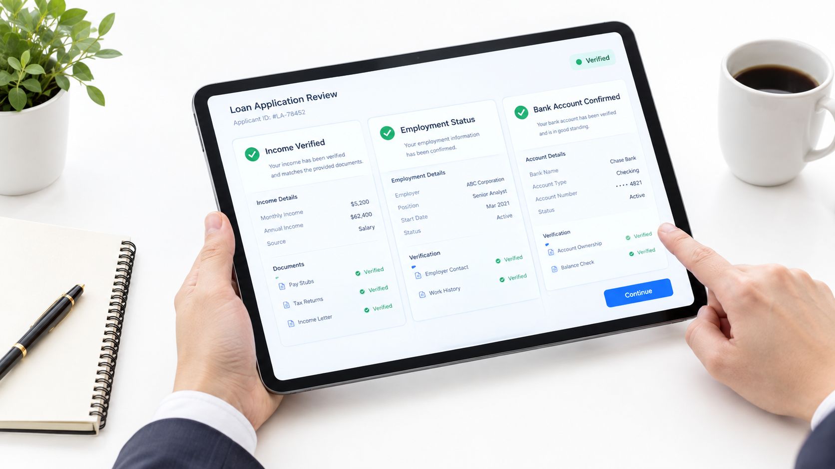 A person reviewing an online loan application status on a tablet held over a white desk surface.